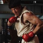 Ein muskulöser Mann mit roten Boxhandschuhen, angespannte Haltung, in einem dunklen industriellen Raum.