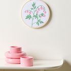 Keine Texte vorhanden. Stickerei mit rosafarbenen Blumenblüten und grünen Blättern, darunter pinke Keramikgegenstände.