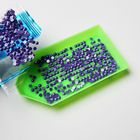 Keine erkennbaren Texte. Ein grünes Tablett, gefüllt mit violetten Pailletten aus einem Plastikbeutel auf weißem Hintergrund.