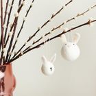 Zwei Filzhäschen hängen an Weidenzweigen in einer rosafarbenen Vase.