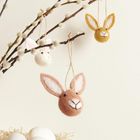 An Zweigen hängen Filzhäschen; unten ein Korb mit weißen Eiern.