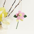 Keine Texte vorhanden. Eine Filzblume in Rosa, Gelb und Grün hängt vor weißen und gelben Papierblumen.