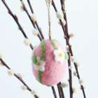 Ein rosa Filzei mit weißen Blüten hängt an einem Ast mit flauschigen Knospen.