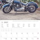 März 2027 Kalender, darunter ein dunkelblaues Motorrad vor einem blühenden Busch und Bäumen.