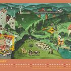 "MÄRZ" oben, Kalender unten. Illustration: Landschaft mit Burg, Bauernhof, Bauarbeiten, Schafen, Surfschule und Zug.