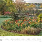 März 2023 Kalender. Ein blühendes Tulpenbeet in einem Garten, umgeben von grünen Bäumen und einem weiten Landschaftshintergrund.