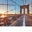 Kalendertext: "2 · 2027". Eine lange Holzbrücke mit Seilen, die bei Sonnenaufgang über den Fluss führt.