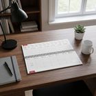 Ein geöffneter Kalender auf einem Schreibtisch zeigt die Tage 11. bis 17. Januar. Daneben Notizbuch, Kugelschreiber, Pflanze.