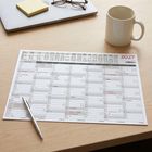 Ein Tischkalender zeigt das Jahr 2027. Daneben ein Stift, eine Tasse, gelbe Haftnotizen und eine Brille.