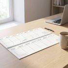 Kalender mit Wochentagen und Daten. Auf einem Tisch mit Laptop, Stift und Tasse. Fenster im Hintergrund.
