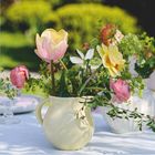 April 2027, Monatskalender. Ein frühlingshaftes Blumenarrangement in einer hellen Vase auf einem Tisch im Garten.