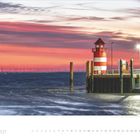 2.2027. Sonnenuntergang mit Leuchtturm am Meer, rote Wolken, Windräder am Horizont, ruhiges Wasser.