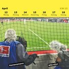 „April 12-18, KW 15, Kameramann, Mikrofon.“ Ein Kameramann filmt ein Fußballspiel hinter einem Netz.