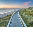 2 · 2027. Ein Holzweg verläuft an der Küste entlang, flankiert von Dünen und einem ruhigen Meer im Sonnenuntergang.