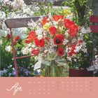 Apr, Monatskalender. Ein Strauß roter Tulpen und weißer Blüten in einer Vase steht auf einem Gartenstuhl.