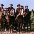 Sechs Cowboys sitzen auf Pferden in einer ländlichen Umgebung.