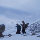 Menschen wandern in einer verschneiten Berglandschaft, dick eingepackt mit Rucksäcken und Gehstöcken bei Schneefall.
