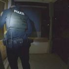 Text: "POLICE". Eine uniformierte Person steht vor einer Tür. Dunkle Umgebung, die Tür ist leicht beleuchtet.