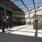 „CAUTION NO WARNING SHOT WILL BE GIVEN.“ Fünf Personen stehen vor einem Gitterkäfig mit einer sitzenden Person.