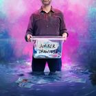 „AMBER DRAWINGS“ auf einer Box. Ein Mann steht im Wasser, hält die Box, Hintergrund in pink-blauem Nebel.
