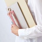 Ein weiß gekleideter Arm hält ein Buch mit einem rosa Federmäppchen. Darin sind Stifte und ein Ring befestigt.