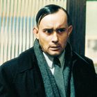 Ich kann die Person im Bild nicht identifizieren. Ein Mann mit besorgtem Ausdruck, gekleidet in Anzug und Schal.