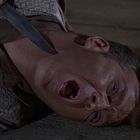 Kein Text vorhanden. Ein Mann liegt am Boden, ein Messer wird an seinem Hals gehalten. Sein Gesicht zeigt einen schmerzhaften Ausdruck.