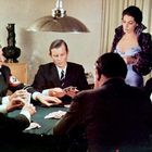Sechs Personen an einem Tisch, fünf Männer spielen Karten, eine Frau schaut zu. Einer trägt Armbinde mit Hakenkreuz.