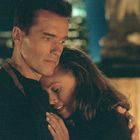 Ein Mann und eine Frau umarmen sich liebevoll, er schaut ernst, sie lächelt leicht. Hintergrund: verschwommene Lichter.