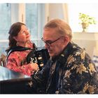 Ein Mann und eine Frau musizieren gemeinsam. Sie spielt Akkordeon, er Klavier. Beide tragen bunte Hemden.