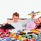 Ein Junge hält ein Lego-Flugzeug, ein Mädchen sitzt daneben, umgeben von vielen bunten Legosteinen.