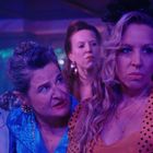 Zu sehen sind mehrere Personen in einem Club, beleuchtet von violettem Licht. Sie blicken ernst oder konzentriert.