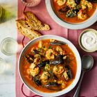 Ein Tischgedeck mit zwei Schalen Meeresfrüchtesuppe, Brot, einem Glas Wasser und einem kleinen Schälchen mit Soße.