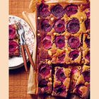Ein braunes Tablett mit frisch gebackenem Pflaumenkuchen und einem Teller mit zwei Stücken daneben, garniert mit Gabeln.