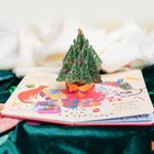 Ein Pop-up-Buch mit einem 3D-Weihnachtsbaum. Rechts steht: "But what might be inside of them, nobody yet knows."