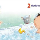 „2 duckies in the tub.“ Ein Kind badet in einer Wanne voller Schaum. Zwei gelbe Enten schwimmen, eine Katze schaut zu.