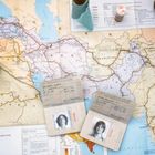Pässe mit Fotos auf einer Weltkarte des Nahen Ostens und Südasien. Objekte wie Fläschchen sind darauf platziert.