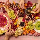 Bunte Speisen auf kariertem Tuch: Radicchio, Brot, Dips in Rosa und Grün, Karotten, Chicorée, Granatapfel und Kräcker.