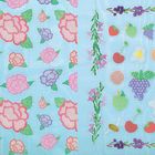 Stickerei-Illustration: Bunte Blumen und Früchte auf hellblauem Hintergrund, mit Blütenmustern und Blättern verziert.