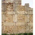 Eine alte Steinmauer aus großen und kleinen Steinen, teils zerfallen, mit Gras am unteren Rand.
