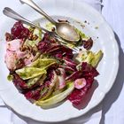 Radicchio- und Chicorée-Salat mit grüner Soße, roten Zwiebeln und Pekannüssen, serviert auf weißem Teller.