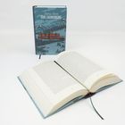 "Thomas Mann DER ZAUBERBERG" auf einem Buchcover mit alpiner Landschaft und einem Gebäude. Ein aufgeschlagenes Buch davor.