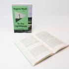 "Virginia Woolf: To the Lighthouse" steht auf einem Buchcover mit Leuchtturm und grüner Landschaft. Ein aufgeschlagenes Buch liegt davor.
