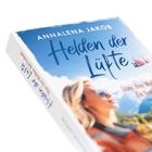 "Helden der Lüfte" von Annalena Jakob; Untertitel: "Über den Wolken wartet die Freiheit." Eine Frau mit Sonnenbrille vor Bergen.