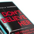 Text: "Nicola Sanders - DON'T BELIEVE HER". Buchcover in Schwarz mit roter Schrift. Weiße Details.