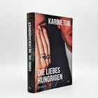 "Karine Tuil: Die Liebeshungrigen. Roman. dtv." Ein elegant gekleidetes Paar, nahe beieinander, eine Hand im Vordergrund.