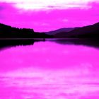 Keine Texte zu erkennen. Ein See mit Bergen im Hintergrund, in magentafarbenen Tönen gehalten.