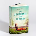 "Sonja Roos, Das Geheimnis der Frauen, Roman. Frau sitzt im Gras unter einem Baum, entspannter Ausdruck, blaue Himmel."