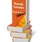 Buchtitel "Bonnie Garmus: Peck & Peck", "Vorläufiges Cover" auf einem orangefarbenen Buchstapel.