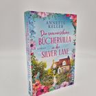 "Die verwunschene Büchervilla in der Silver Lane" von Annette Keller. Ein Haus, umgeben von bunten Blumen.